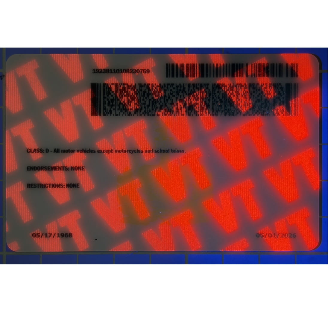 A close-up of a red and black holographic decal or sticker with repeating stylized lettering and barcode/serial text, photographed against a dark blue background.